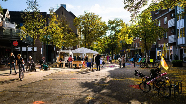 Menschen genießen eine verkehrsberuhigte Straße mit Fahrrädern, Sitzgelegenheiten und einem Zelt bei einer Stadtteilaktion.