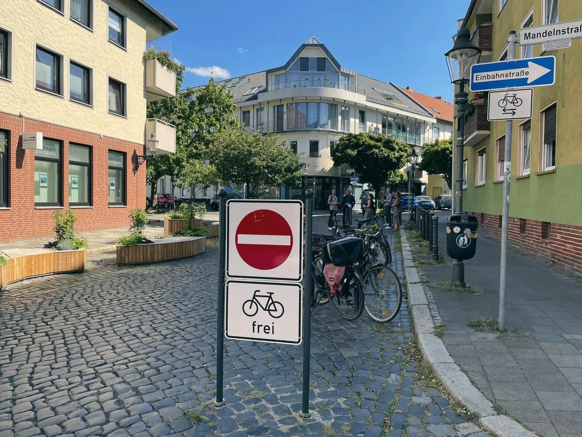 Eine für den Radverkehr freigegebene Einbahnstraße im Quartier, dahinter abgestellte Räder und Menschen auf dem Gehweg.