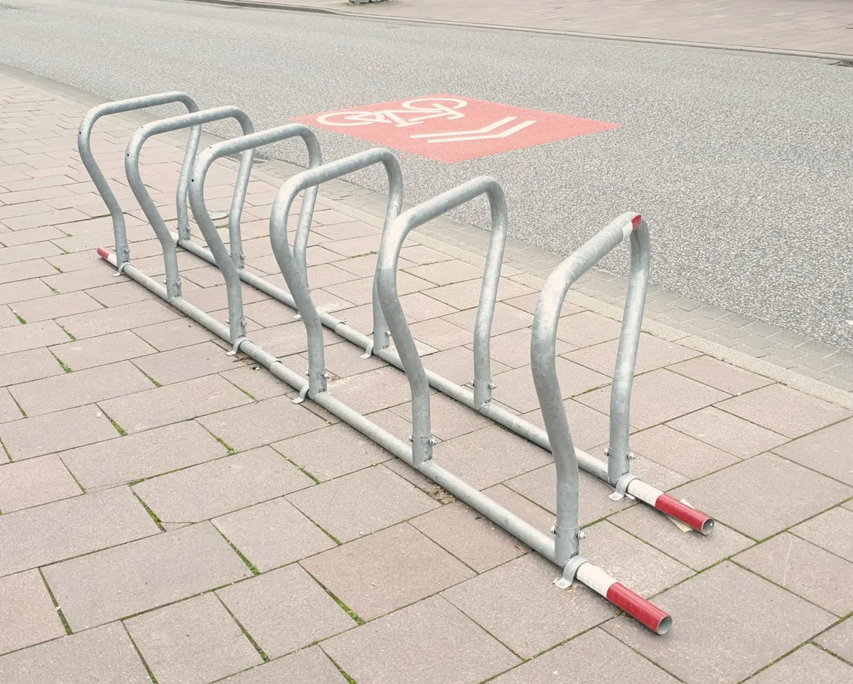 Ein mobiler Fahrradständer aus verzinktem Stahl steht am Gehwegrand neben einem Radfahrstreifen.