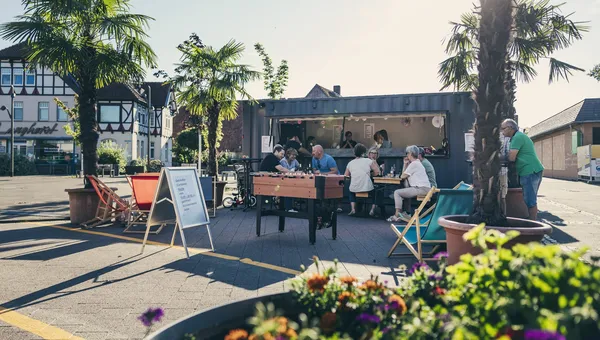 Ein Gastro-Container mit Kickertisch, Liegestühlen und Pflanzkübeln auf einem umgestalteten Platz.