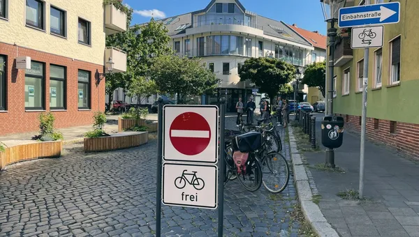 Eine für den Radverkehr freigegebene Einbahnstraße im Quartier, dahinter abgestellte Räder und Menschen auf dem Gehweg.