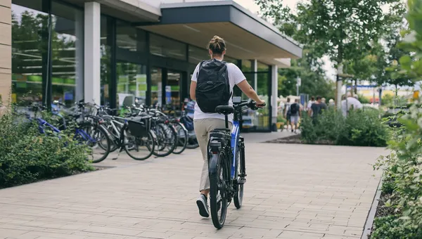 Eine Frau, von hinten gesehen, schiebt ihr Rad auf einen Anlehnbügel am Gehweg zu.
