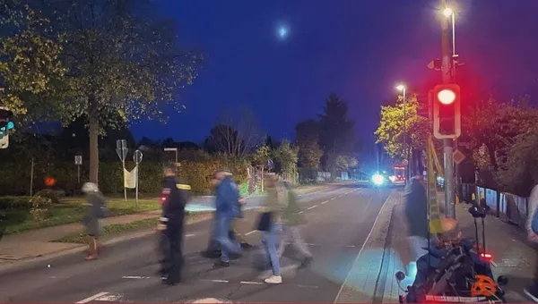 Menschen queren am Abend eine Hauptstraße an einer Fußgängerampel, die Rot zeigt.