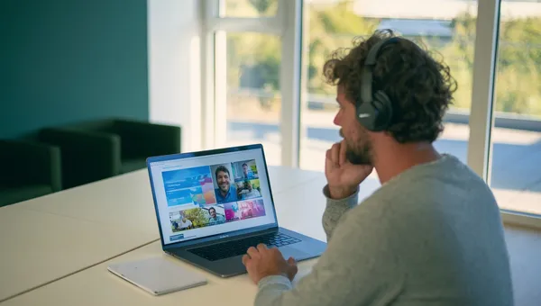 Eine Person mit Kopfhörern verfolgt am Laptop eine Videokonferenz.