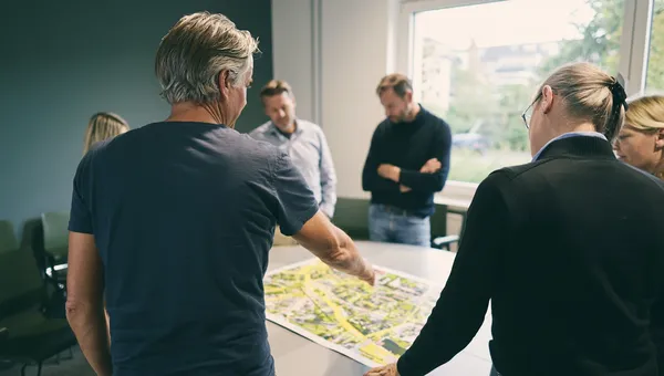 Mehrere Personen stehen um einen Tisch und besprechen einen ausgebreiteten Plan.