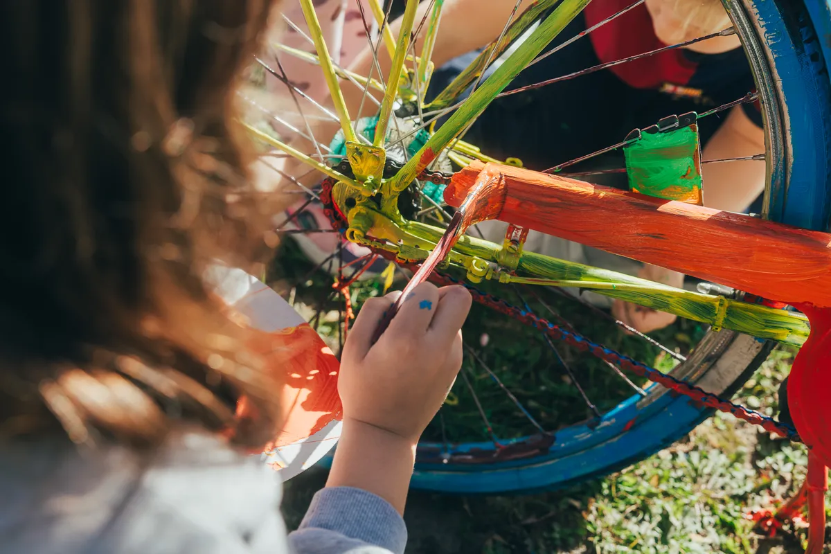 Eine Kinderhand bemalt einen Fahrradrahmen mit bunter Farbe.