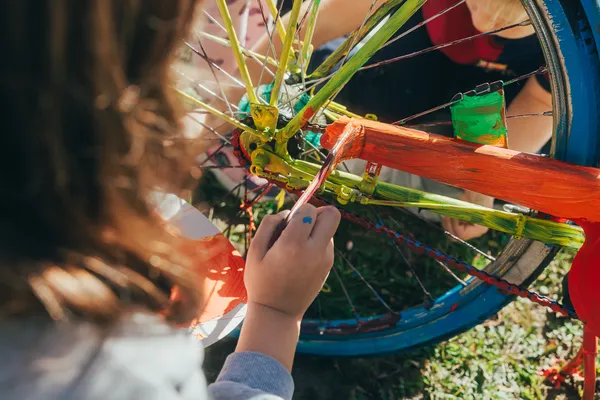 Eine Kinderhand bemalt einen Fahrradrahmen mit bunter Farbe.
