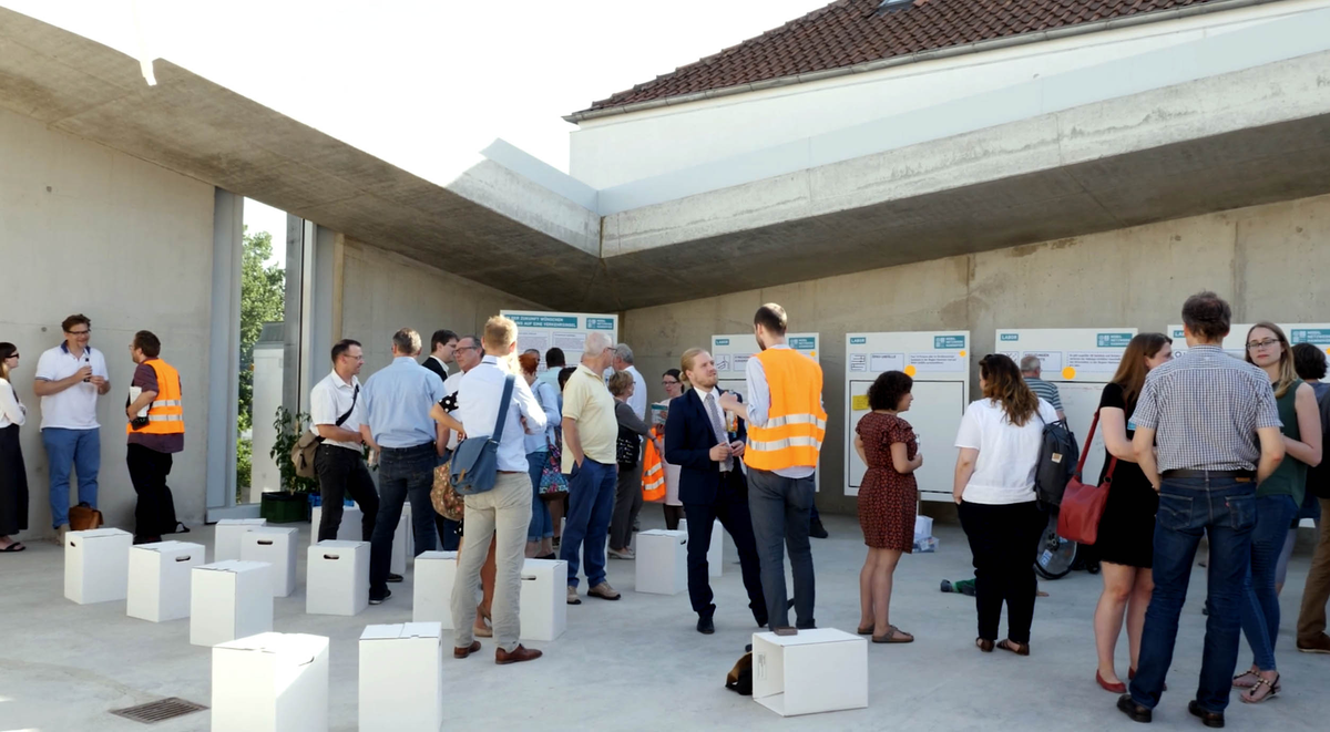 Menschen tauschen sich bei einer Veranstaltung im Freien vor Infotafeln aus.