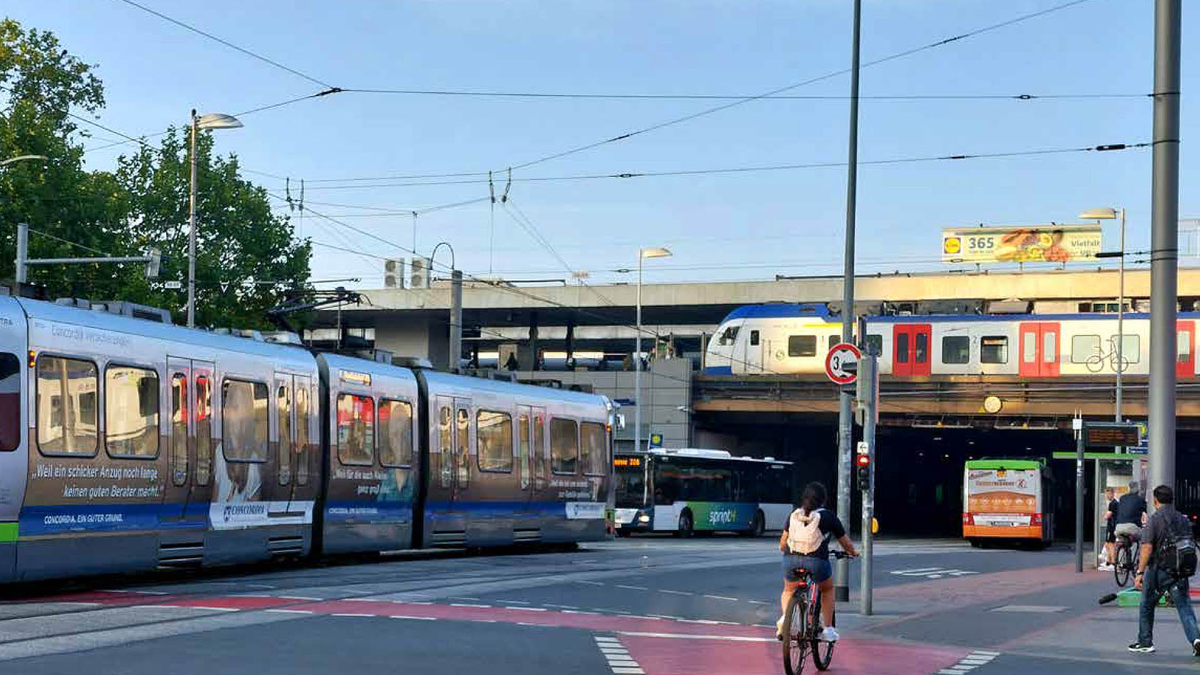Straßenbahn, S-Bahn, Busse und Radfahrende an einer großen Kreuzung in Hannover.