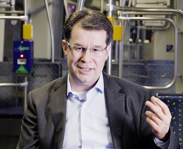 Mann mit Brille spricht in einer Straßenbahn und gestikuliert mit der Hand.