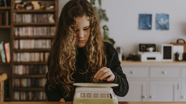 Kind wirft eine Münze in eine VW-Bus-Spardose in einem gemütlichen Wohnzimmer.