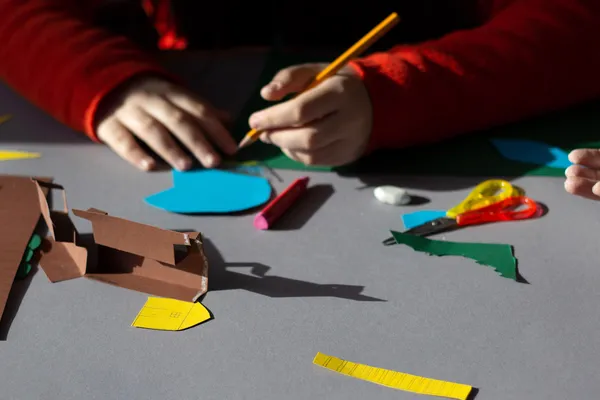 Kinderhände basteln mit farbigem Papier, Schere und Holzbausteinen an einer Mitmachstation.