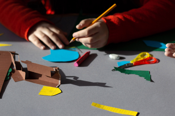 Kinderhände basteln mit farbigem Papier, Schere und Holzbausteinen an einer Mitmachstation.
