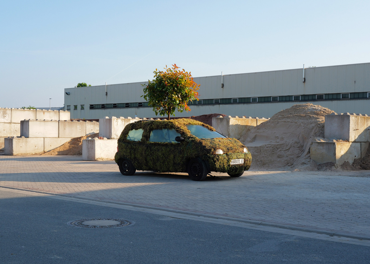 Ein vollständig mit Pflanzenmatten begrüntes Auto mit einem Baum auf dem Dach.